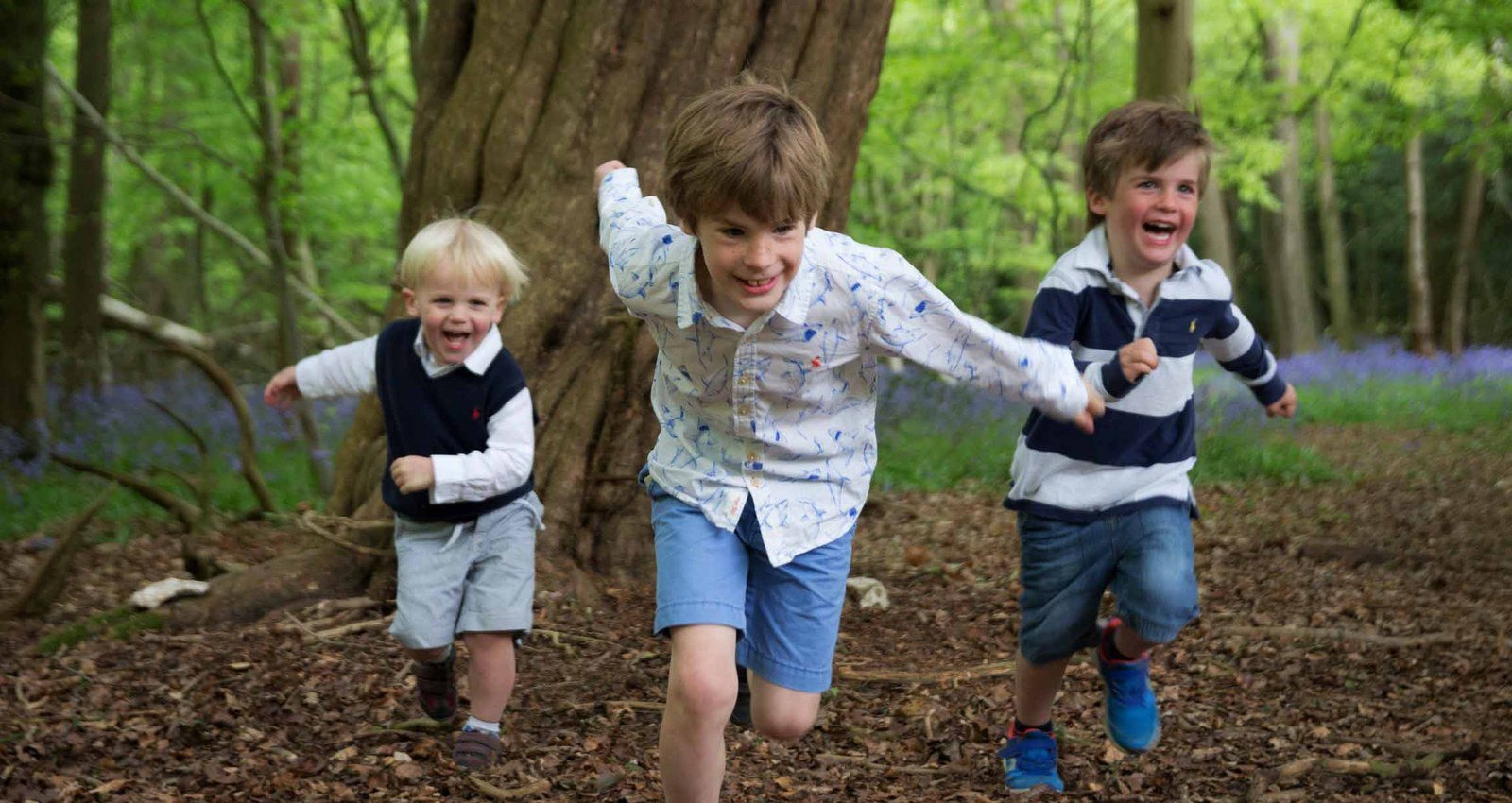 Three children running through a bluebell wood